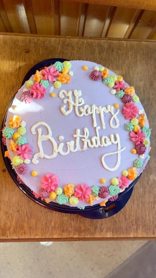 Gâteau d'anniversaire mauve entouré de petites fleurs colorées