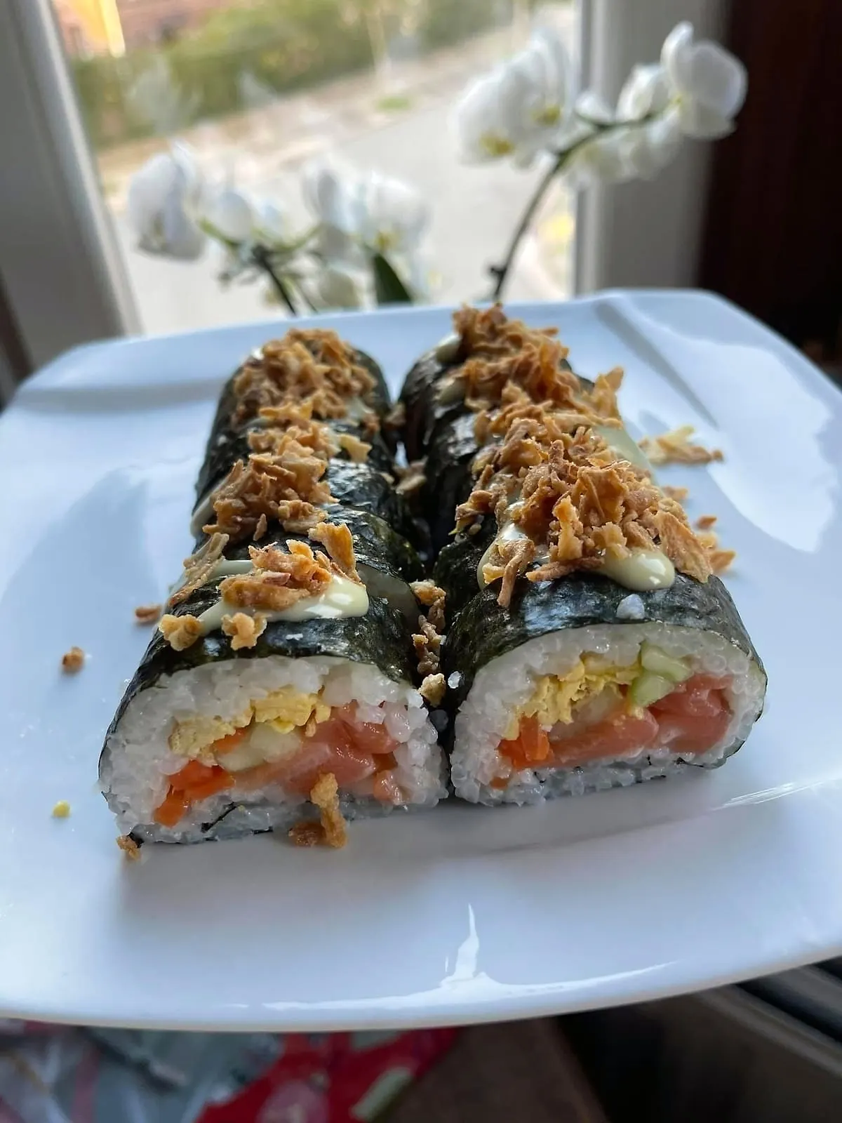 Makis au saumon garnis d'oignons frits, dressés sur une assiette